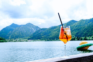 A glass of Aperol against the backdrop of mountains and a lake. Summer holidays Schliersee.