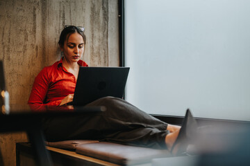 Focused young business entrepreneur working on her laptop in a casual indoor setting, using technology for productivity.