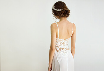 young brunette sexy girl in a white wedding boudoir dress and jewellery in hairstyle is standing...