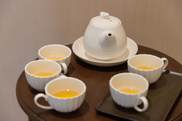 A white tea set with four cups and a teapot on a wooden table