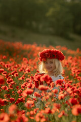 A young girl is standing in a field of red poppies. She is wearing a red headband and holding a red...