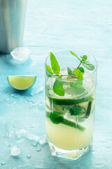 Mojito cocktail in a highball glass. Summer cold drink with lime, fresh mint, and ice. Cool beverage on a blue background