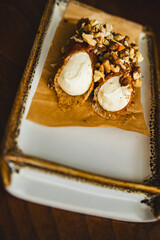 Two cannoli on a plate with. The cannoli are filled with cream and topped with nuts. The plate is a simple white ceramic plate with a brown border.