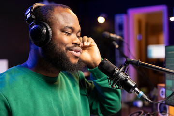 Confident songwriter performing a tune on microphone in home studio, recording his song and editing...