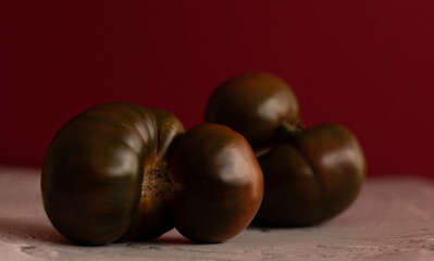 Tomate kumato sobre mesa blanca con fondo rojo