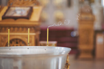 Candle and smoke in church. Christian church. Orthodox baptism bowl of holy water and candles.