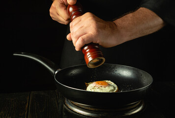 Cooking delicious scrambled eggs in the kitchen. A chef adds pepper to a hot pan of eggs while...