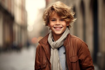 Fototapeta premium Portrait of a cheerful boy with curly hair, wearing a stylish jacket and scarf outdoors