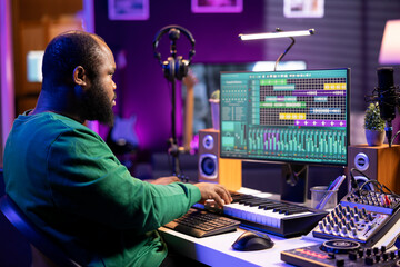 Sound engineer recording piano notes with DAW software in his home studio, working at night on...