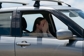 A woman sitting in a car covers her face with her hands, showing signs of stress or frustration....