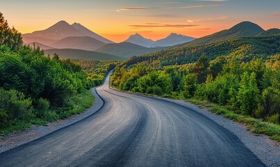 Fototapeta premium An empty asphalt road meandering through a verdant forest, with the peaks of distant mountains visible on the horizon