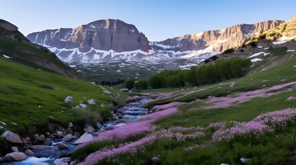 Scenic mountain valley with a meandering stream, vibrant pink wildflowers, lush greenery, and majestic snowy peaks under a clear blue sky.
