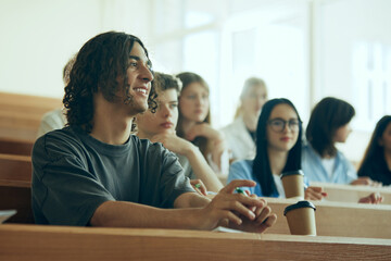 Young students, boys and girls sitting in university auditorium and listening to lecture. Growing...
