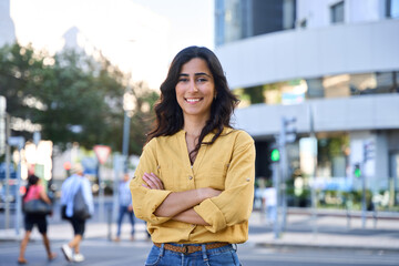 Smiling portrait of middle eastern Israel girl with crossed arms at busy city urban street. Young...