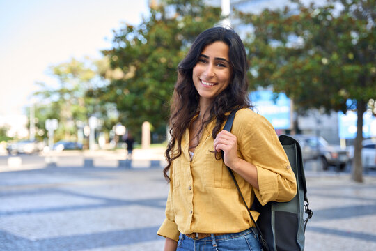 Smiling portrait of beautiful middle eastern Israel girl student with backpack looking at camera at campus city urban background. Young Arabian or Indian woman standing at street outdoor, copy space