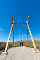 a man swings on a giant tourist swing between mountains and meadows. Curious place Liérganes,...