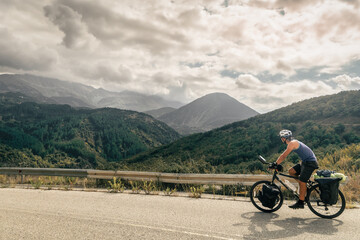 Caucasian cyclist solo bicycle touring around mountains in summer with scenic mountain rage...