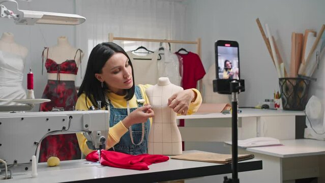 Young fashion designer demonstrates to her subscribers and students how to measure a mannequin's chest circumference. She is filming this tutorial for her sewing blog.