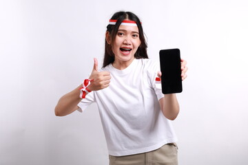 A cheerful Asian woman wearing red white headband, showing her phone while gesturing OK sign with her fingers, isolated by white background. Indonesia's independence day concept