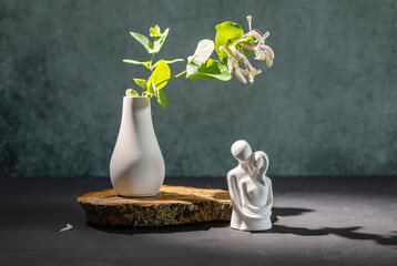  interior composition of a flowering honeysuckle twig and a plaster statuette of a family on a...