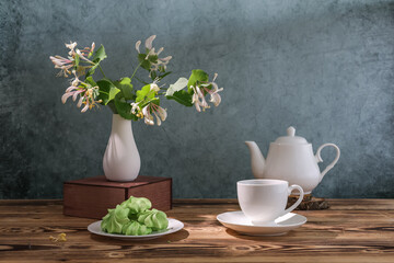 cup of tea with marshmallows from aquafaba and a sprig of honeysuckle Caprifol on a wooden table