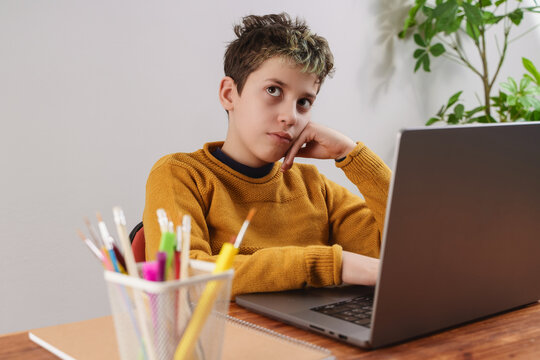 Distracted Boy Studying on Laptop sitting at desk - Contemplative Student During Online Learning
