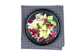 Vegan leafy vegetable salad on black plate top view isolated on white