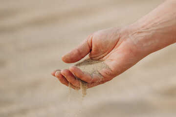 A man's hand pouring sand in the desert in Qatar