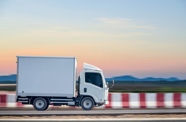 Small white truck for transport on the road against the evening background.