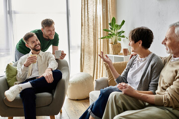 A gay couple sits with parents on a couch, enjoying a conversation and a cup of coffee.