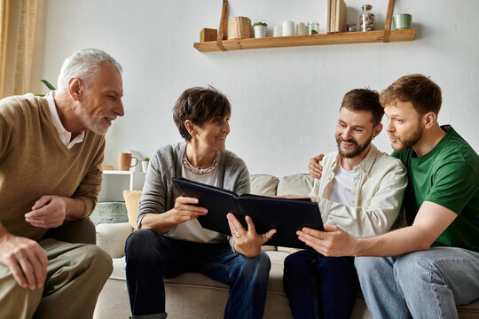 A gay couple sits on a couch with parents, sharing photos from a photo album.