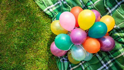 lots of colorful birthday balloons on a checkered blanket on the lawn in summer