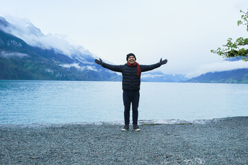 Fototapeta premium An asian man standing at the edge of Lake Brienz in Switzerland admiring the view of the alps