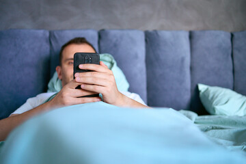 a young man scrolls in smartphone in the morning after waking up, morning routine