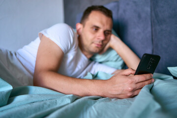 a young man scrolls in smartphone in the morning after waking up, morning routine