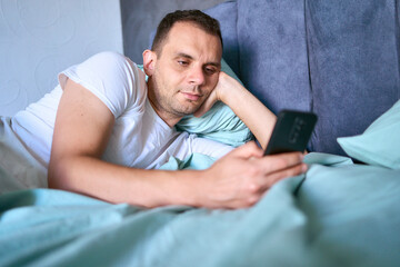 a young man scrolls in smartphone in the morning after waking up, morning routine