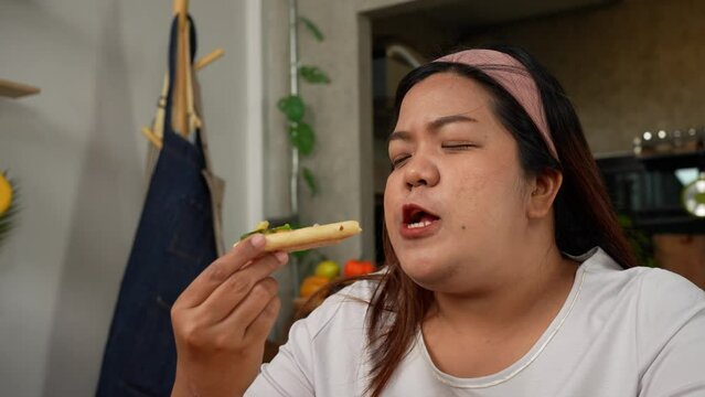 Happy Asian woman eating homemade pizza in home after baked pizza. Overweight women enjoy eating. Concept of binge eating disorder BED and Relaxing with Eating junk food and unhealthy foods.