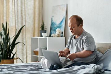 A man with inclusivity sits on his bed, engrossed in his laptop.