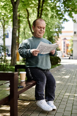 Obraz premium A man with inclusivity sits on a park bench reading a newspaper and enjoying a cup of coffee.