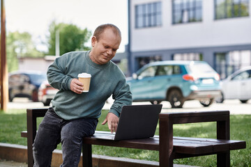 Fototapeta premium A man with inclusivity sits on a park bench, enjoying coffee and using a laptop on a sunny day.