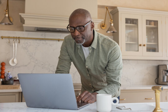 Senior man at home in his kitchen using a laptop for online banking