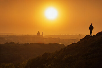 Fototapeta premium Person steht auf einem Berg / Hügel bei Sonnenuntergang und blickt über eine Landschaft