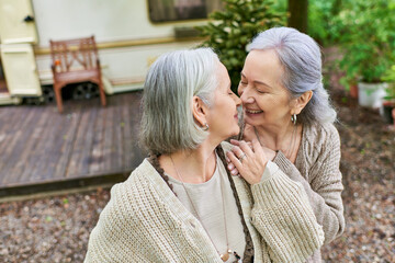 A lesbian couple enjoys a romantic moment while camping in a lush green forest.