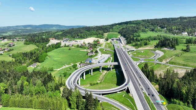 Poland. New Zakopianka multilane highway with a tunnel, multilevel spaghetti junction, crossroad with traffic circles, viaducts, entrance and exit ramps and traffic near Skomielna Biala. Aerial wiew