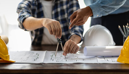 Brainstorming group of architects and engineers discuss building blueprint design on laptop and construction project planning on wooden table in office.