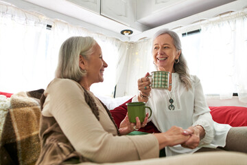 Two women, a lesbian couple, relax in a camping van, enjoying coffee and conversation.