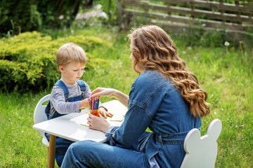 Mother and kid coloring outdoors together. Early years. Baby development.