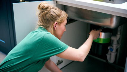 Female Plumber Fixing Waste Disposal Unit In Domestic Kitchen Sink