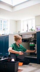 Female Plumber With Digital Tablet Fixing Waste Disposal Unit In Domestic Kitchen Sink