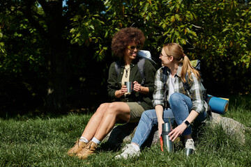 Two young women, a lesbian couple, sit on a rock in a forest, enjoying a break during their hike.